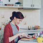 Happy young mother cooking vegetables cutting tomatoes and talking to her cheerful daughter in the kitchen at home. Family, cook, and people concept